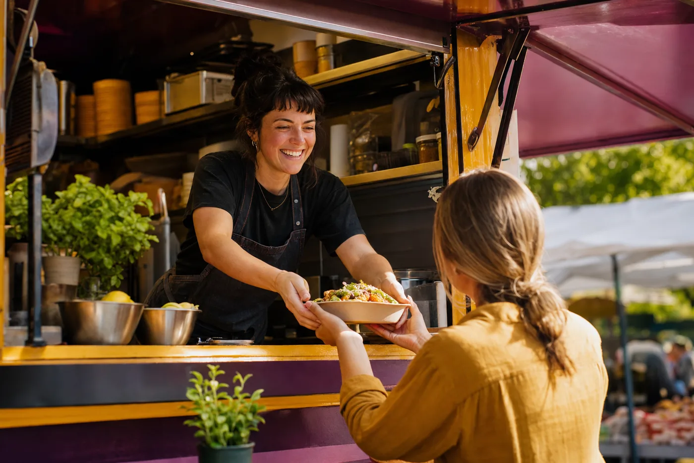 A food truck cook handing a fresh bowl to a customer at a market